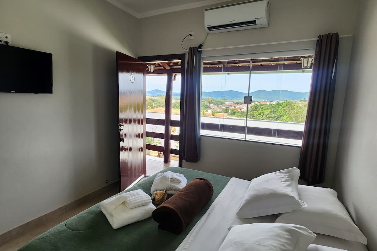 Une chambre d’hôtel équipée d’un lit, d’un téléviseur à écran plat, d’un système de climatisation et offrant une vue sur un paysage montagneux par la fenêtre.