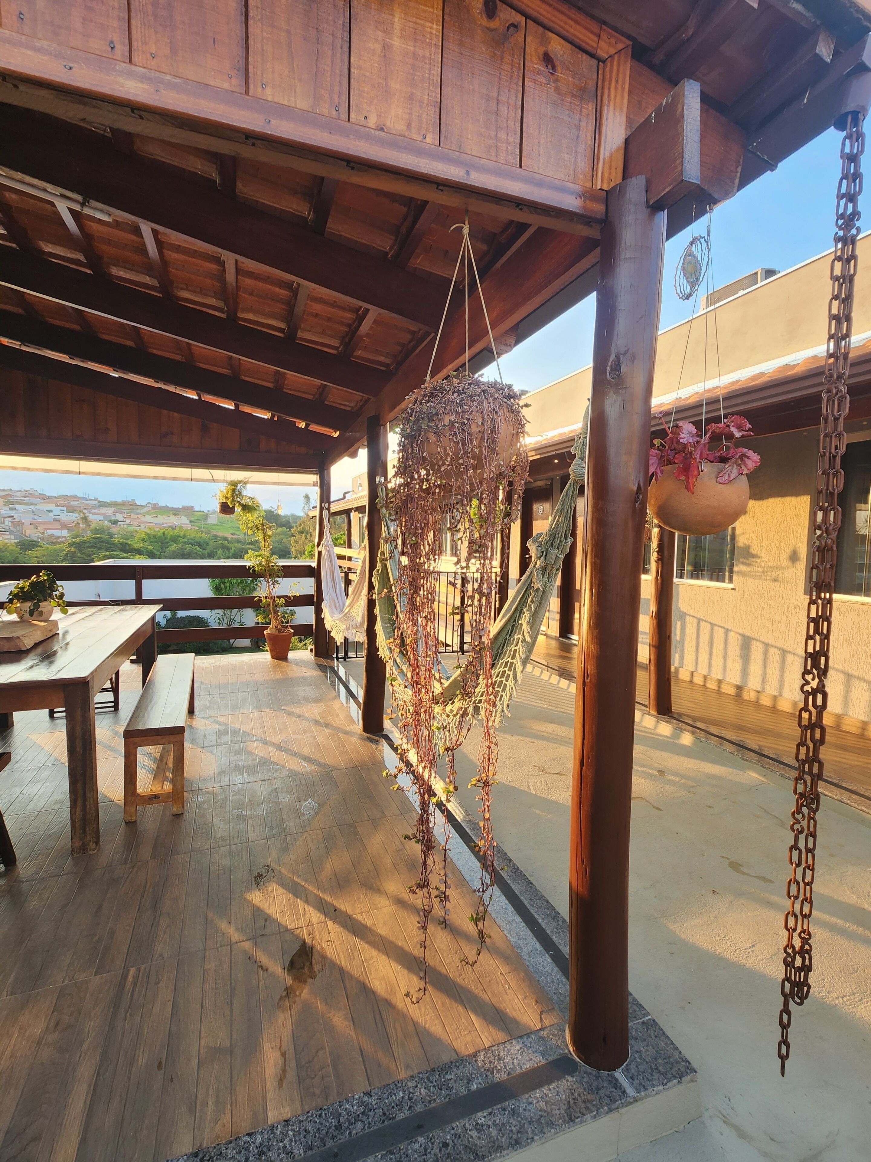 Una terraza de madera con una hamaca, plantas colgantes y vistas a un pueblo.