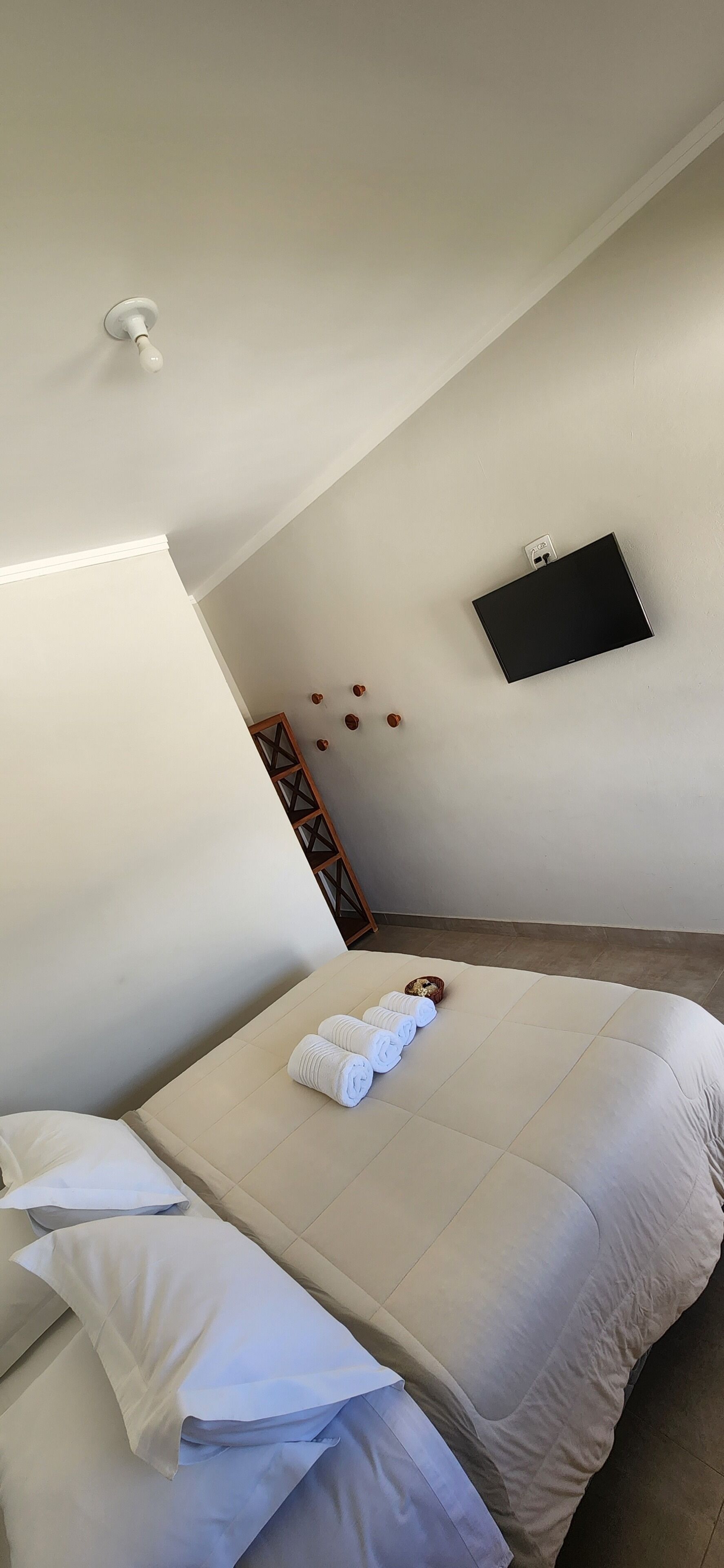 A neatly made bed with white linens, a flat-screen TV mounted on the wall, and a small wooden ladder against the wall.