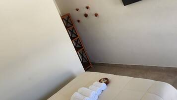 Una cama bien tendida con sábanas blancas, un televisor de pantalla plana montado en la pared y una pequeña escalera de madera apoyada contra la pared.