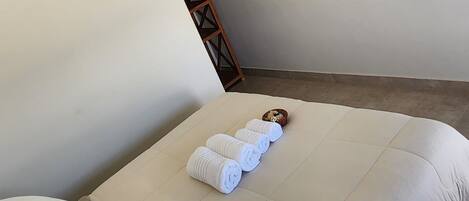 A neatly made bed with white linens, a flat-screen TV mounted on the wall, and a small wooden ladder against the wall.