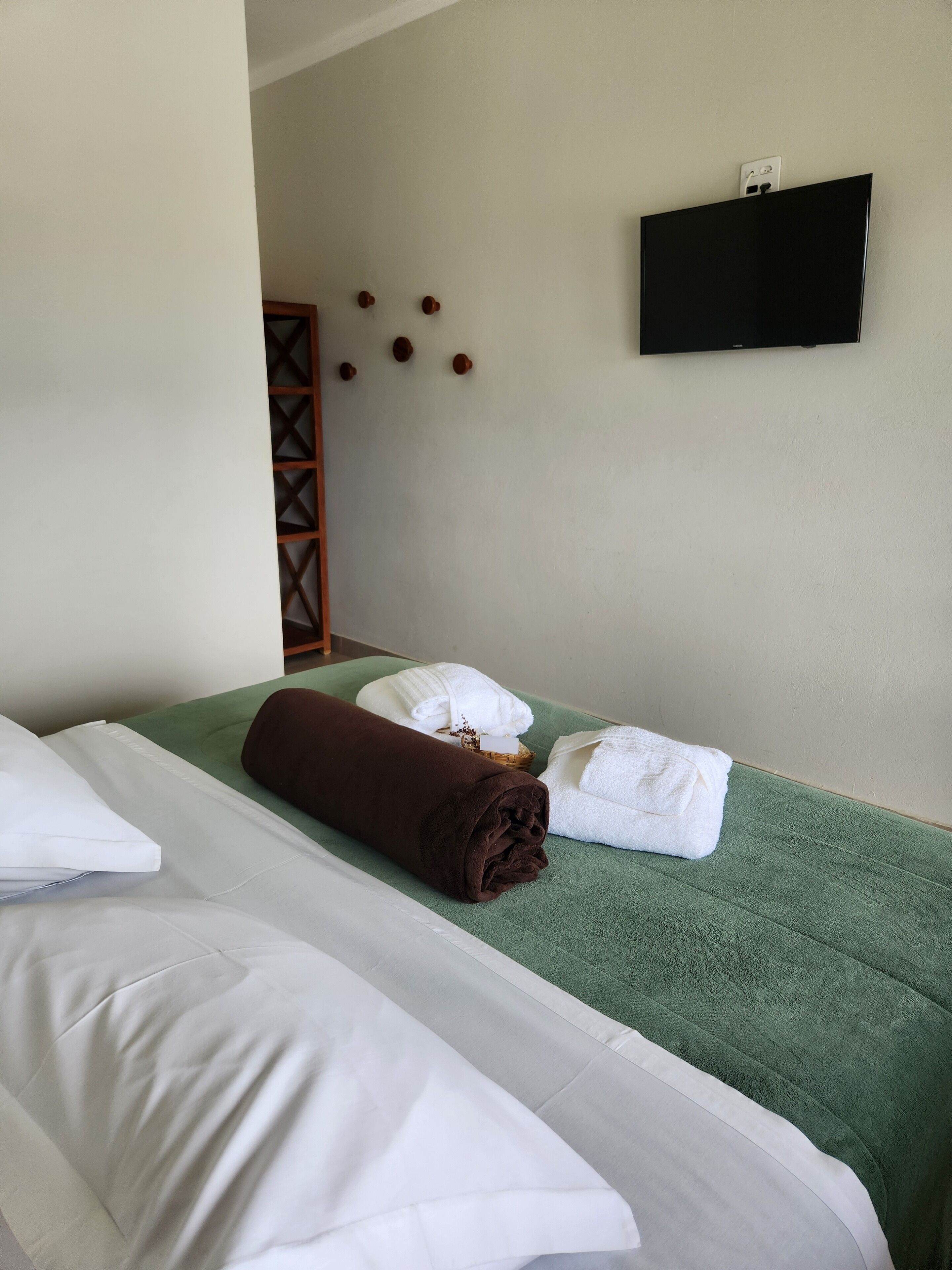 Habitación de hotel con dos camas, toallas verdes y un televisor de pantalla plana en la pared.