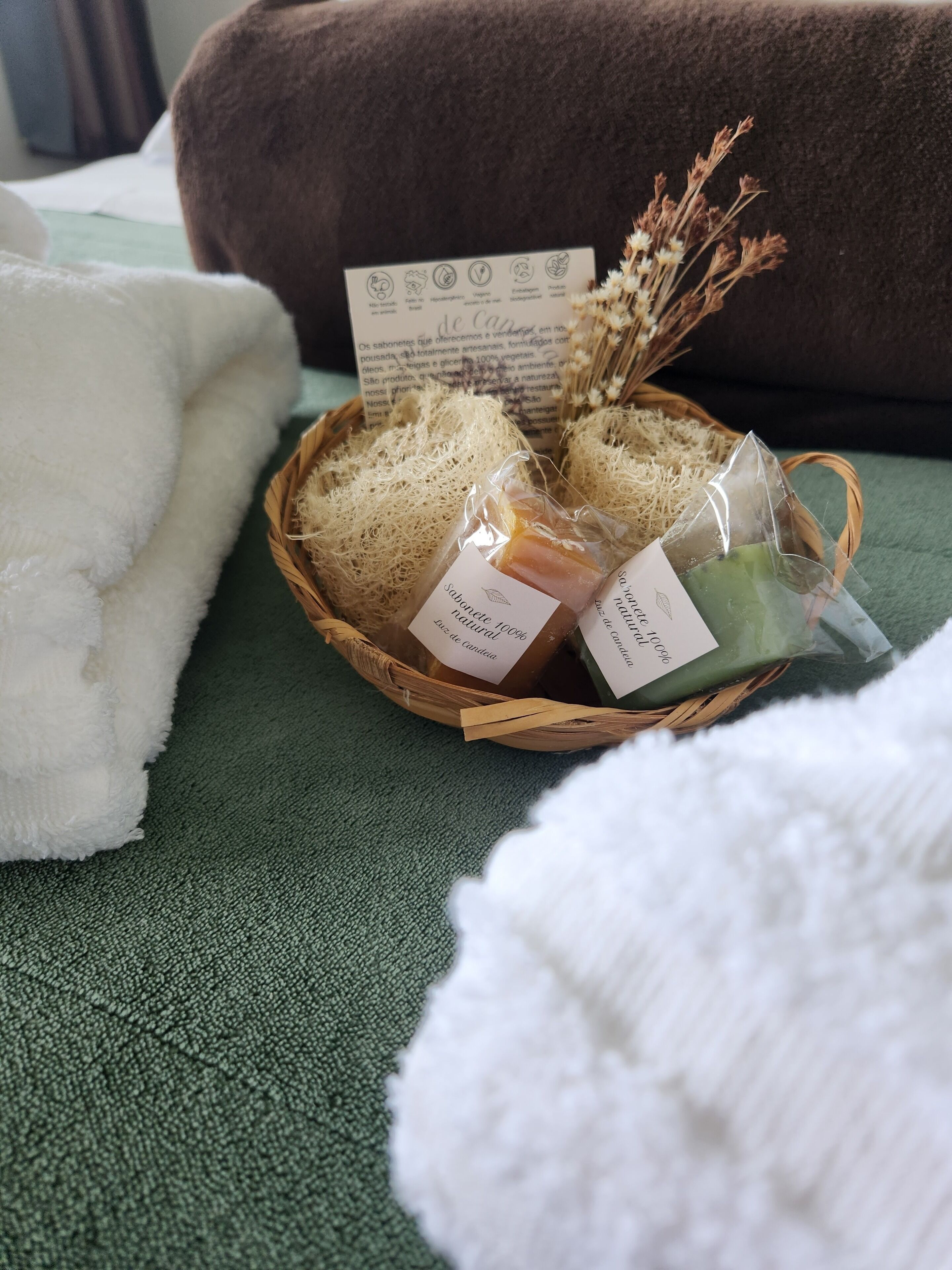 A basket of natural soaps on a green textured surface, with a white towel and a brown cushion in the background.
