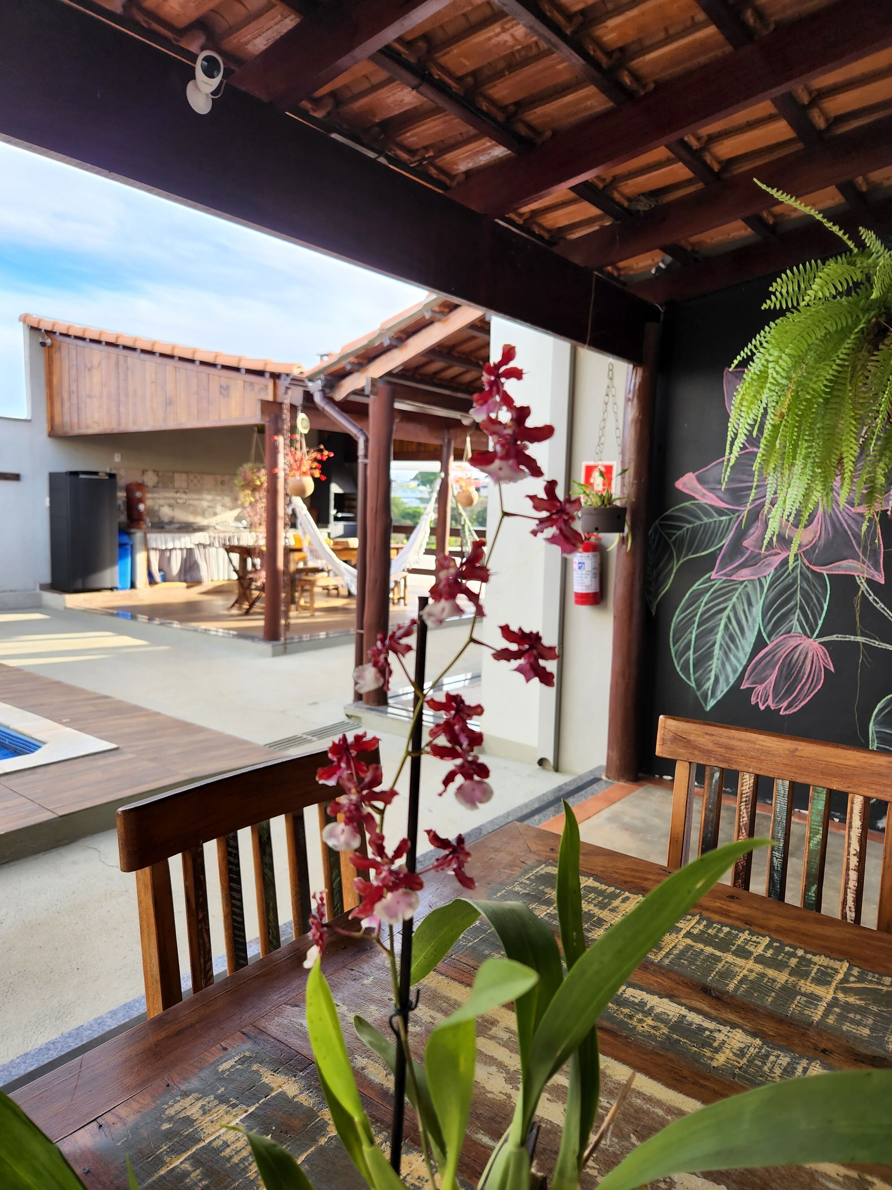 A covered outdoor area with wooden benches, a pool, and a mural of tropical leaves.