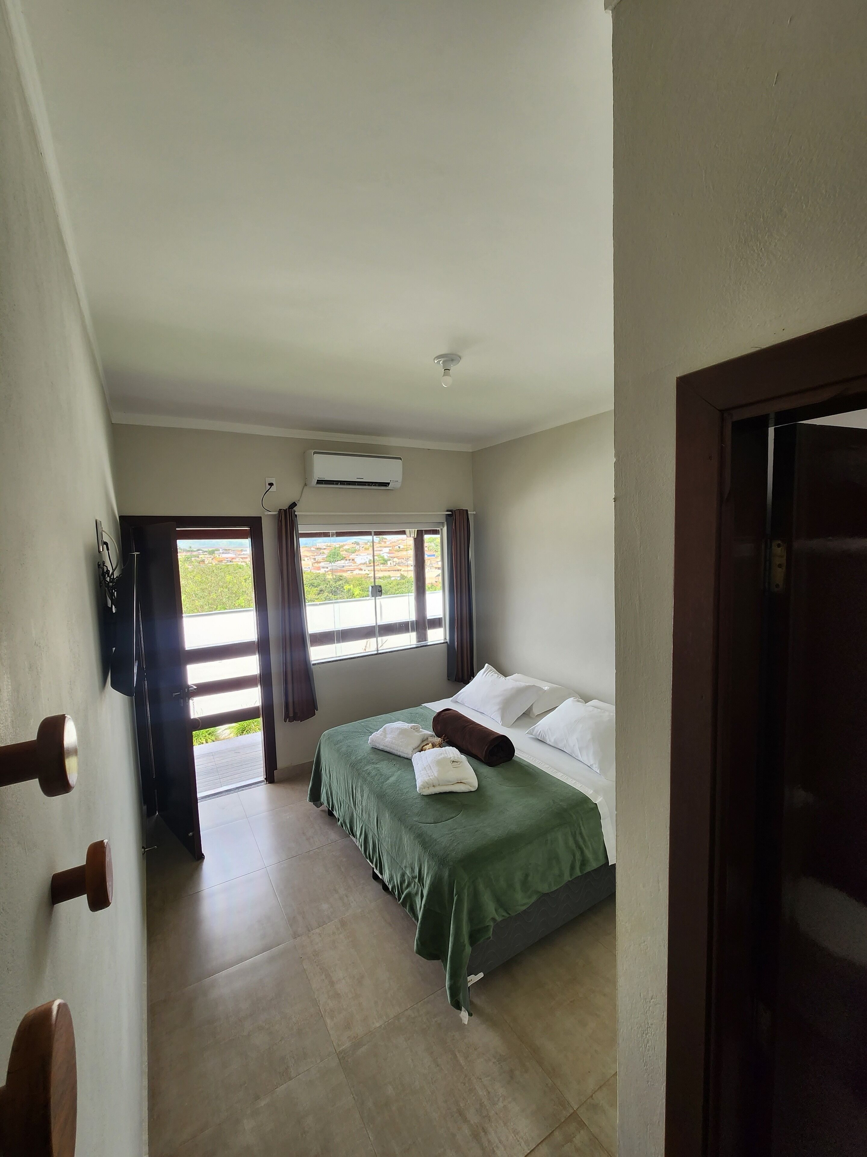 Una camera d'albergo con un letto, una finestra con tende, una ventola a soffitto e un condizionatore d'aria.