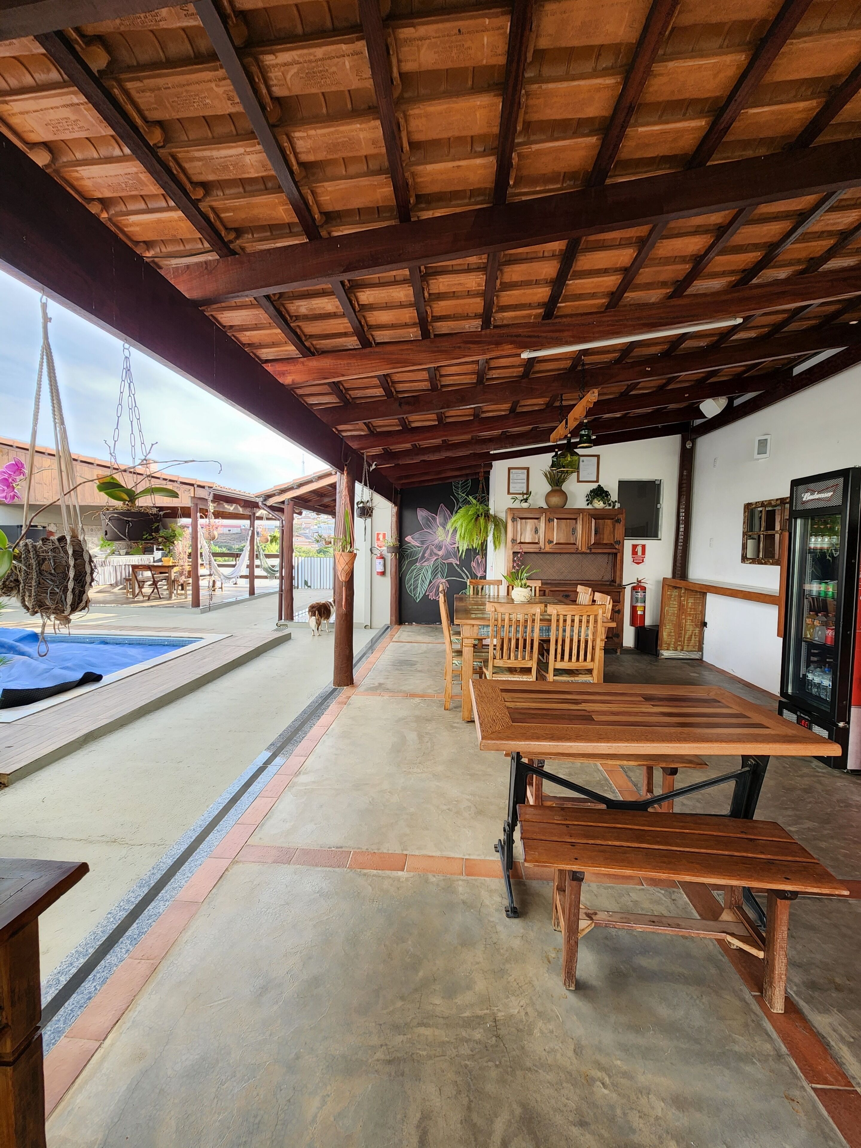 An outdoor patio area with a wooden table and chairs, a pool, and various potted plants.