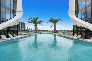 Relax by the pool with a view of the city skyline, surrounded by lounge chairs and palm trees.