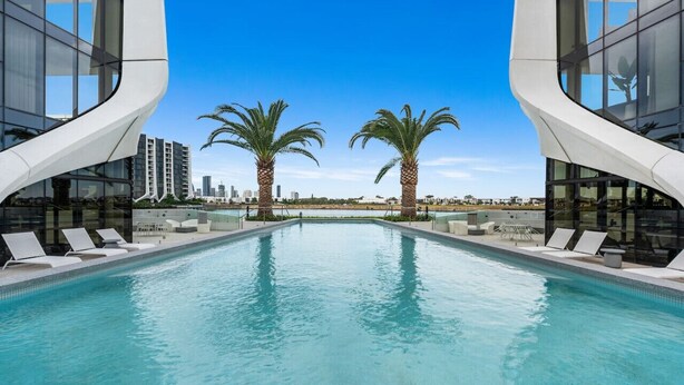 Ein moderner Poolbereich mit zwei Palmen, Liegestühlen und einer Stadtkulisse im Hintergrund.