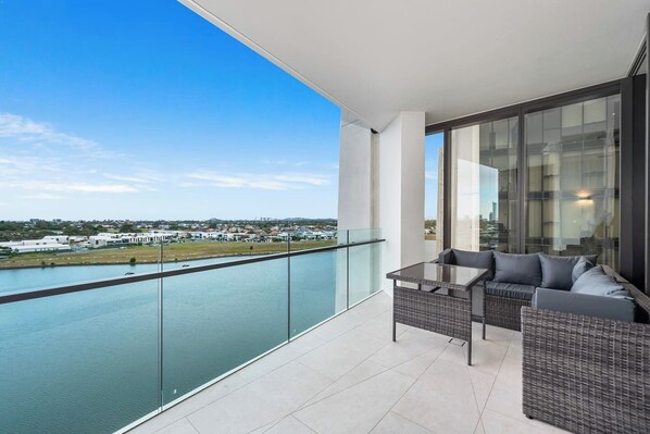 Enjoy breathtaking views of the water and surrounding landscape from this balcony, featuring a wicker sofa and glass-top table.