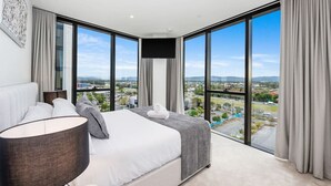 Ein modernes Hotelzimmer mit einem großen Bett, einem Flachbildfernseher und Blick auf die Stadt durch raumhohe Fenster.