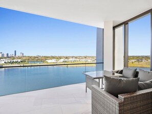 Enjoy a serene view of the water and city from this spacious balcony with a wicker sofa and glass table.