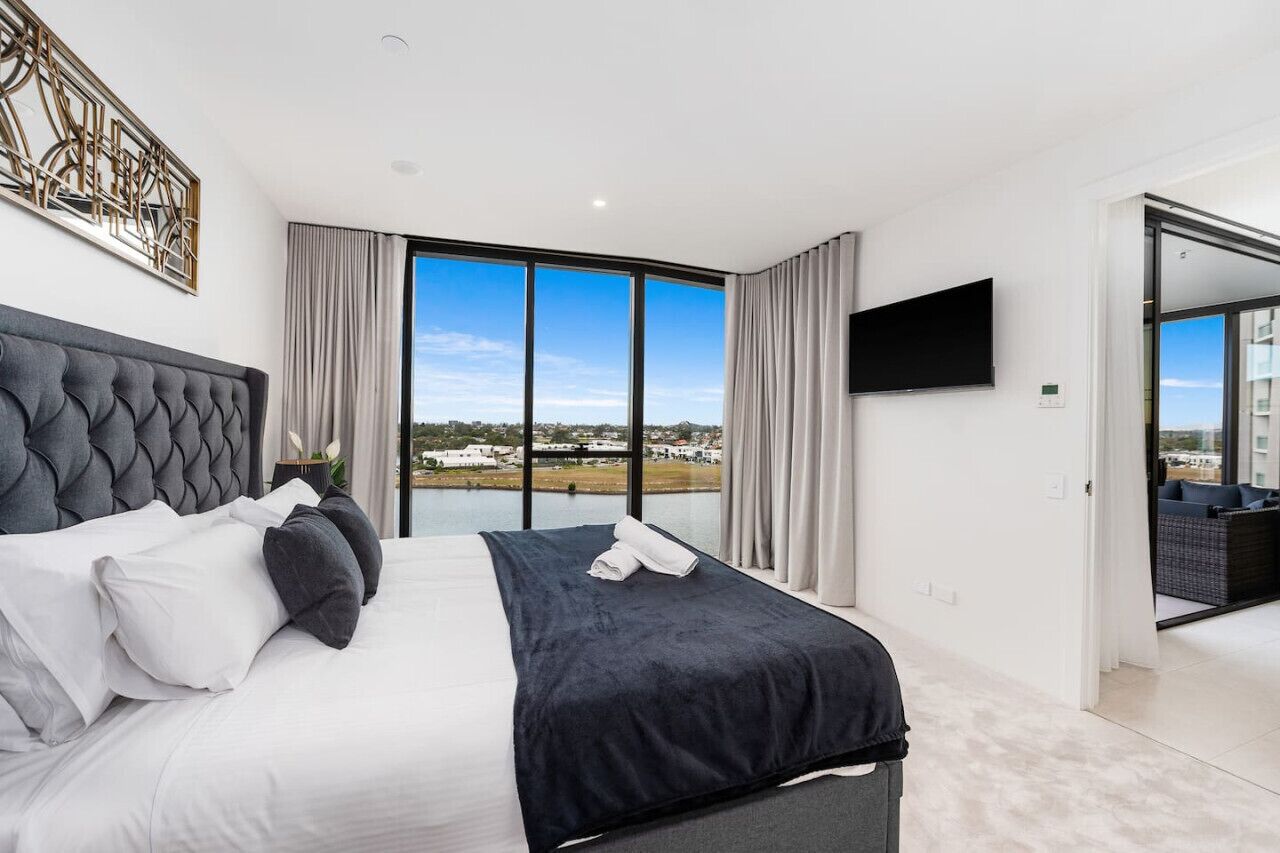 Habitación de hotel moderna con una cama grande, un televisor de pantalla plana y vistas a un paisaje urbano a través de amplias ventanas.