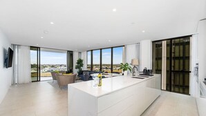 Eine moderne Küche mit einer großen Kochinsel, einem Essbereich inklusive Sofa und Stühlen sowie großen Fenstern mit Blick auf die Stadt.