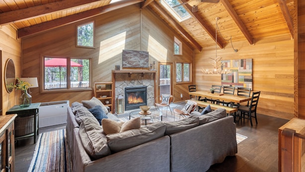 A spacious living room with a fireplace, wooden ceiling, and large windows.