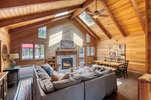 A spacious living room with a fireplace, wooden ceiling, and large windows. - Basecamp at Black Butte (Sisters)