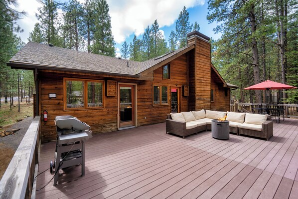 A wooden cabin with a deck, a grill, a sofa, and a fire pit. - Basecamp at Black Butte (Sisters)