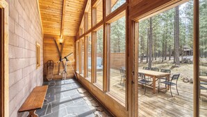 A wooden cabin interior with a stone floor, large windows, a wooden deck, and outdoor seating.