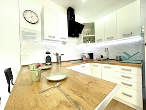 A modern kitchen with white cabinets, a wooden countertop, a sink, a microwave, and a clock on the wall. - Apartamento D&L Precioso Apartamento Recién Reformado (Costa del Silencio)