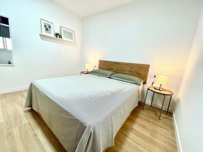 A bedroom with a bed, two bedside lamps, a wooden headboard, and a small shelf with framed pictures. - Apartamento D&L Precioso Apartamento Recién Reformado (Costa del Silencio)