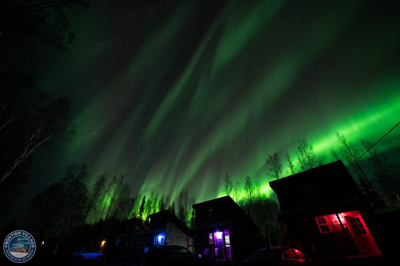Una casa con porche delantero y garaje, rodeada de árboles bajo un cielo nocturno con luces aurorales verdes.