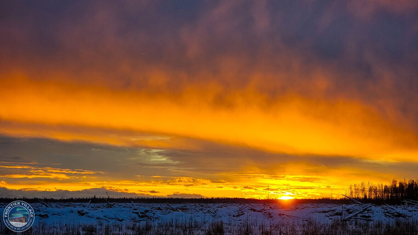 A sunset over a snowy landscape with a forest in the distance.