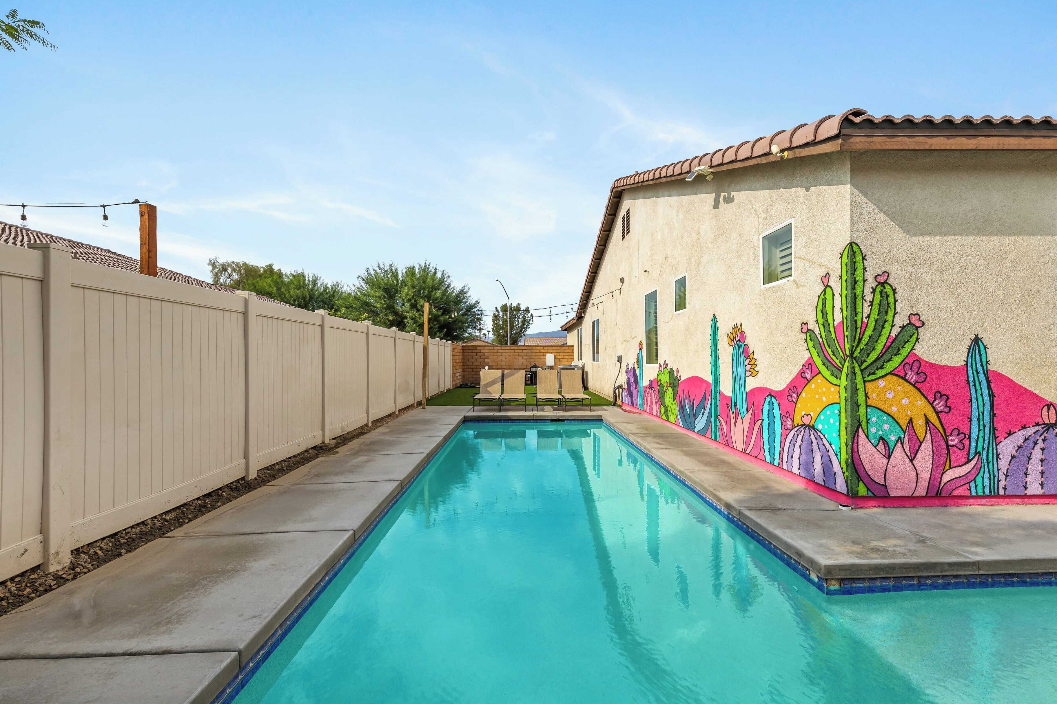 Una piscina con un mural de cactus y flores en la pared contigua.