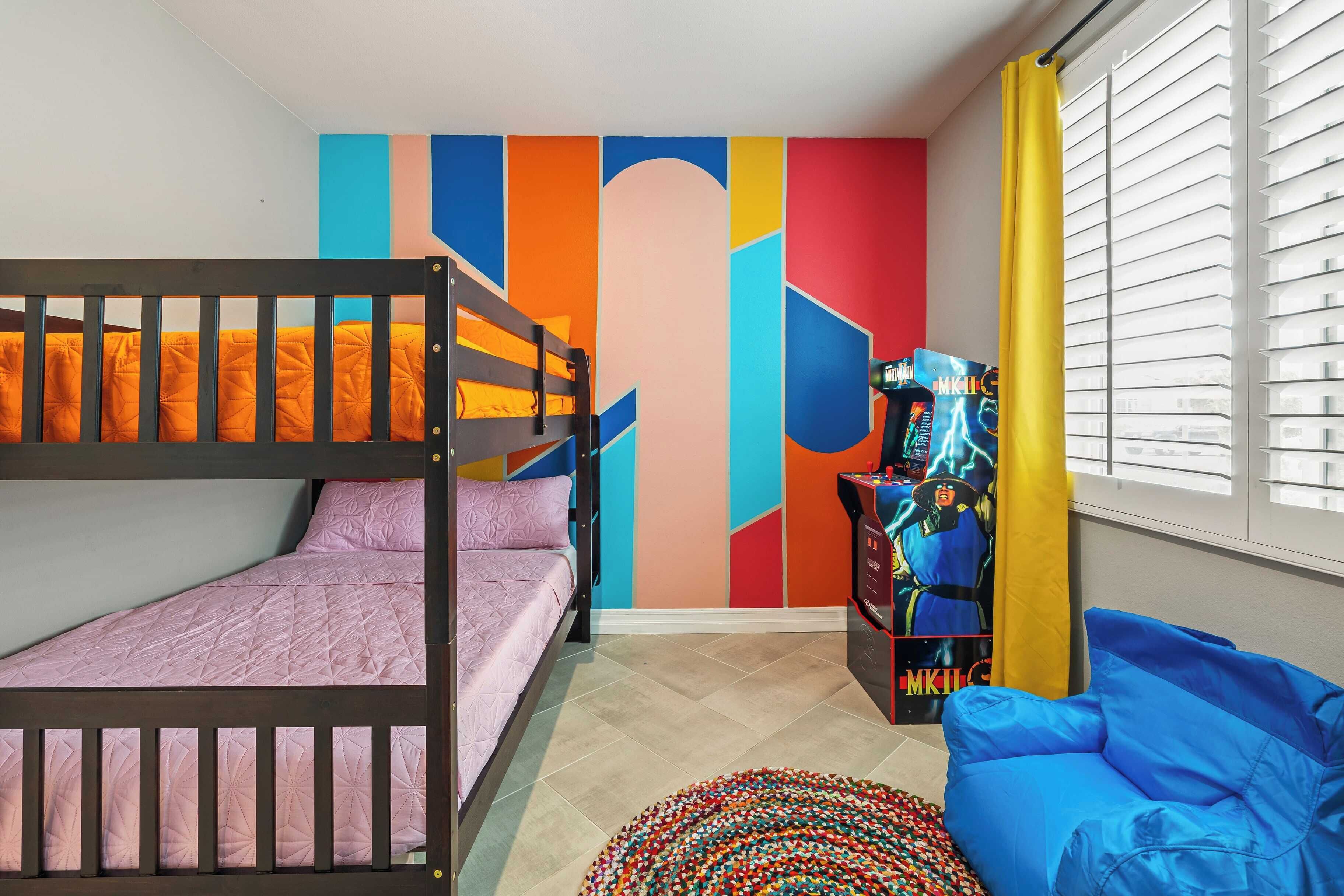 A room with bunk beds, a colorful wall, a gaming console, and a blue chair.