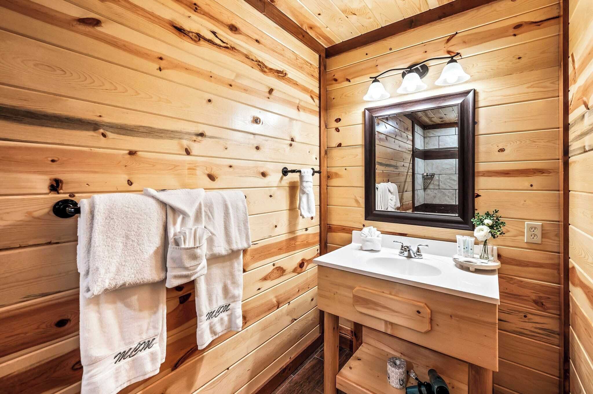 Ein Badezimmer im Holzblockhaus-Stil mit Holzwand, einem großen Spiegel, einem Waschbecken und Handtüchern, die an einem Ablagegestell hängen.