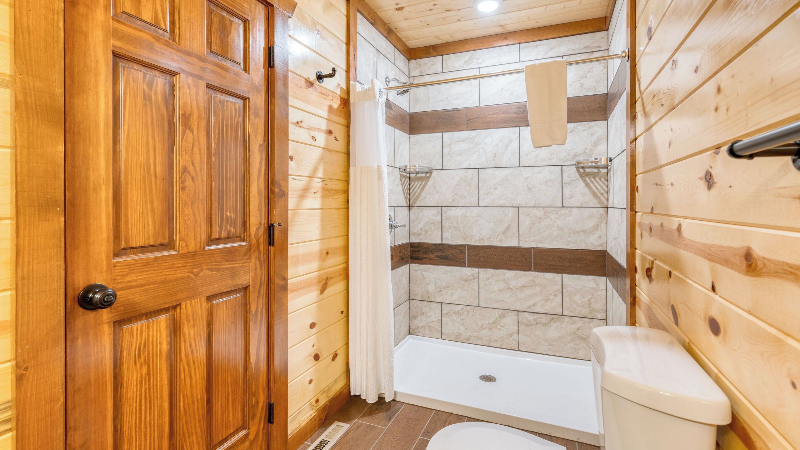 A wooden-paneled bathroom with a bathtub, toilet, and shower area.