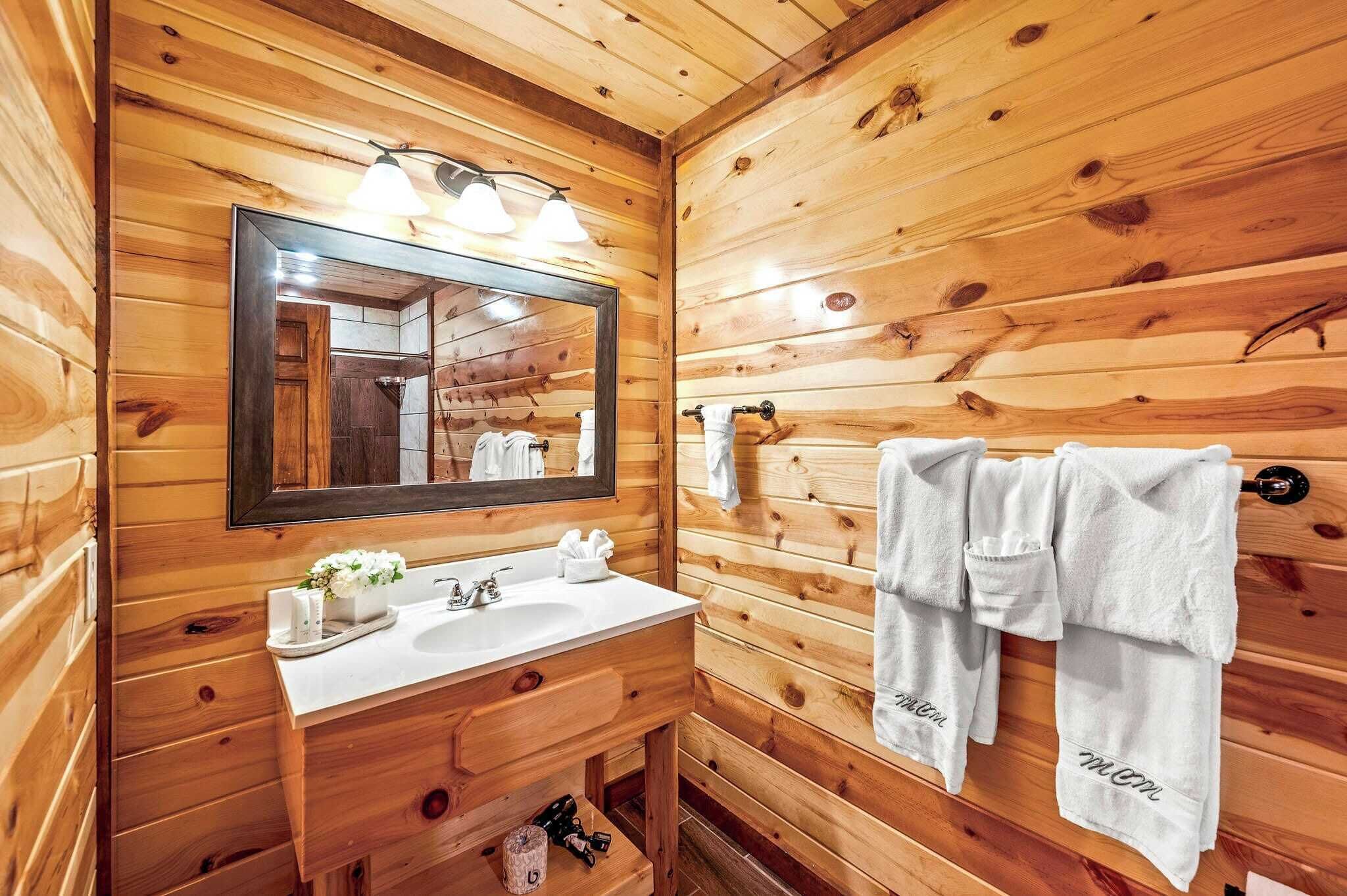 Une salle de bain rustique, avec des murs en bois, un grand miroir, deux lavabos et des serviettes accrochées au mur.