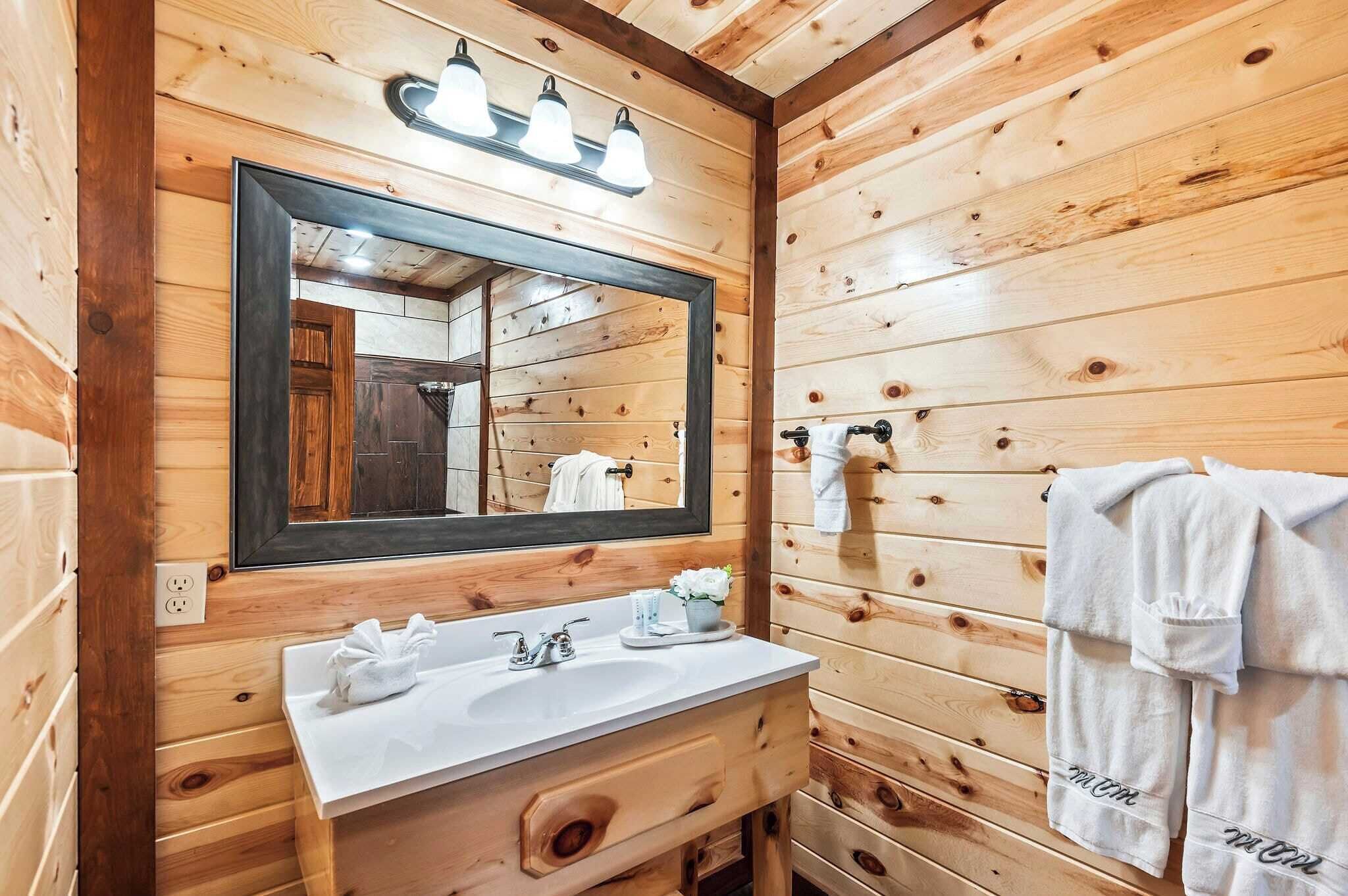 Ein Badezimmer einer Holzhütte mit einem großen Spiegel, einem Waschbecken und einem Handtuchhalter.