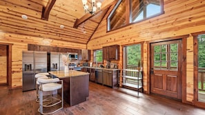 A log cabin-style kitchen with a central island, stainless steel appliances, and a large window overlooking greenery.