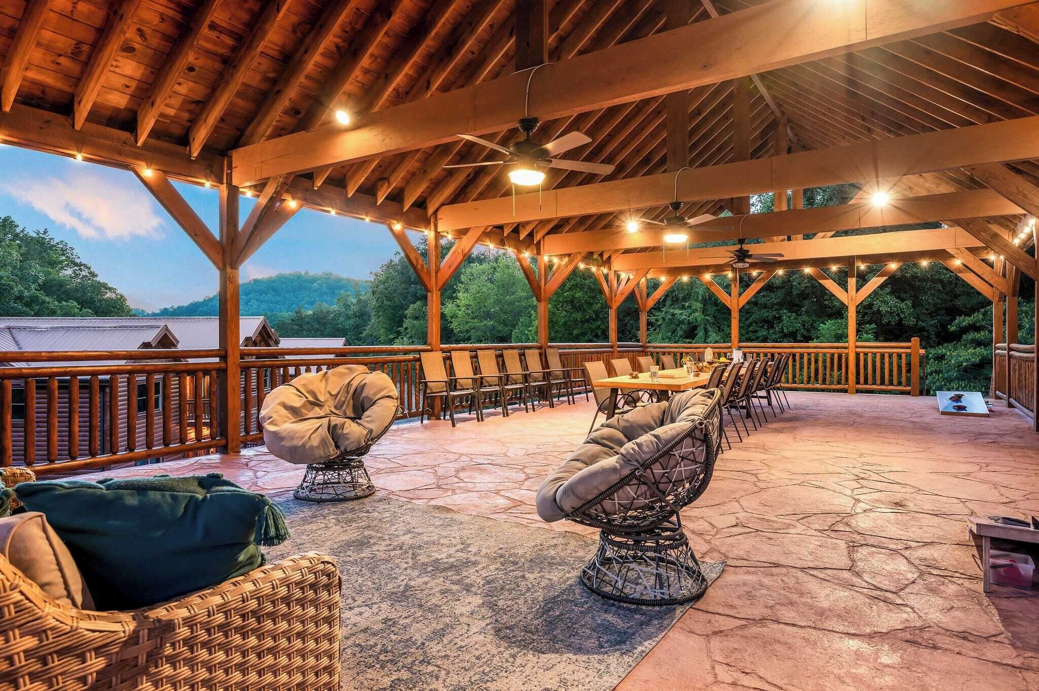 An outdoor covered patio with wooden beams, string lights, wicker furniture, and a stone floor.