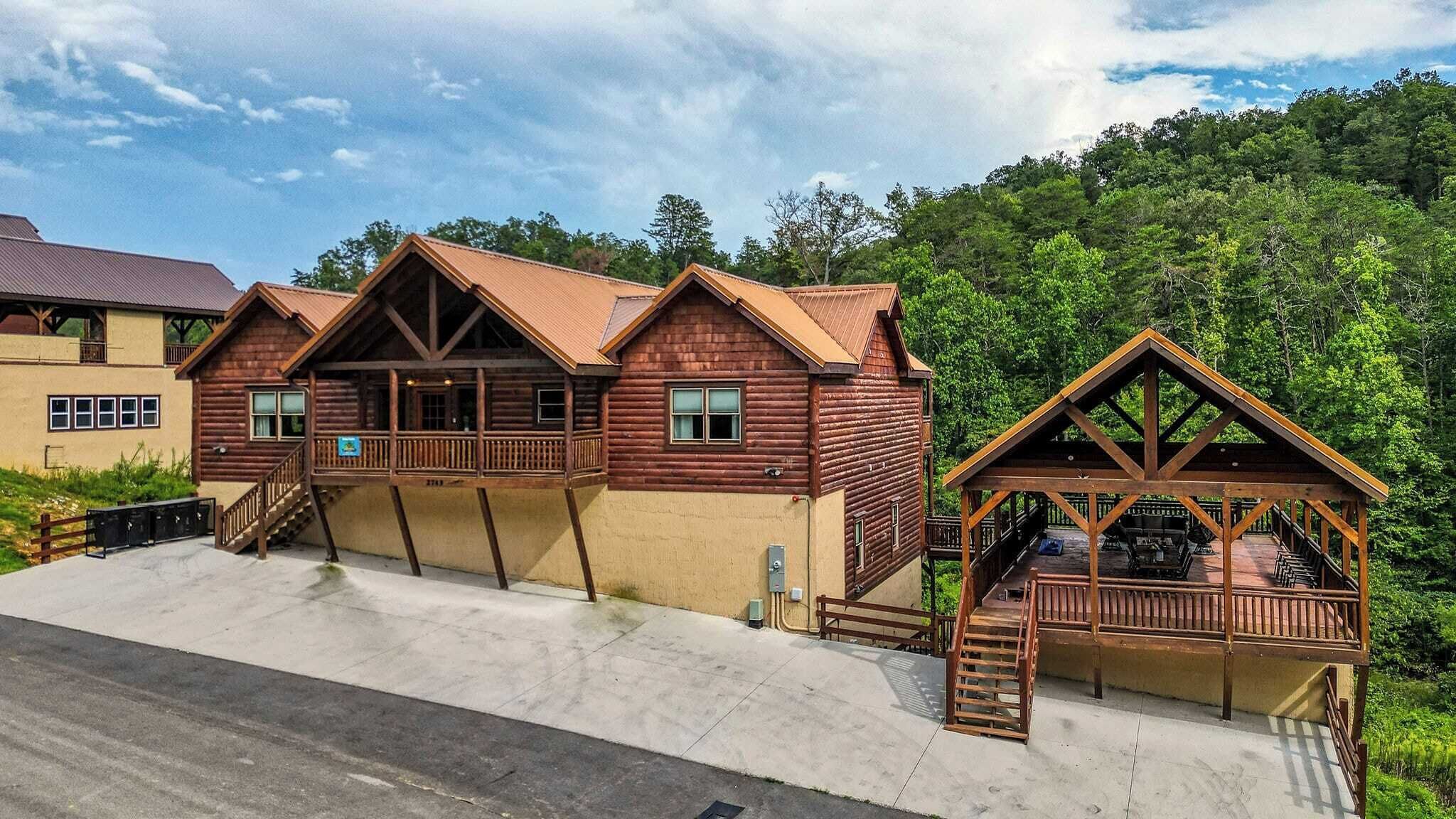 A log cabin with a porch and a covered deck, surrounded by lush greenery.