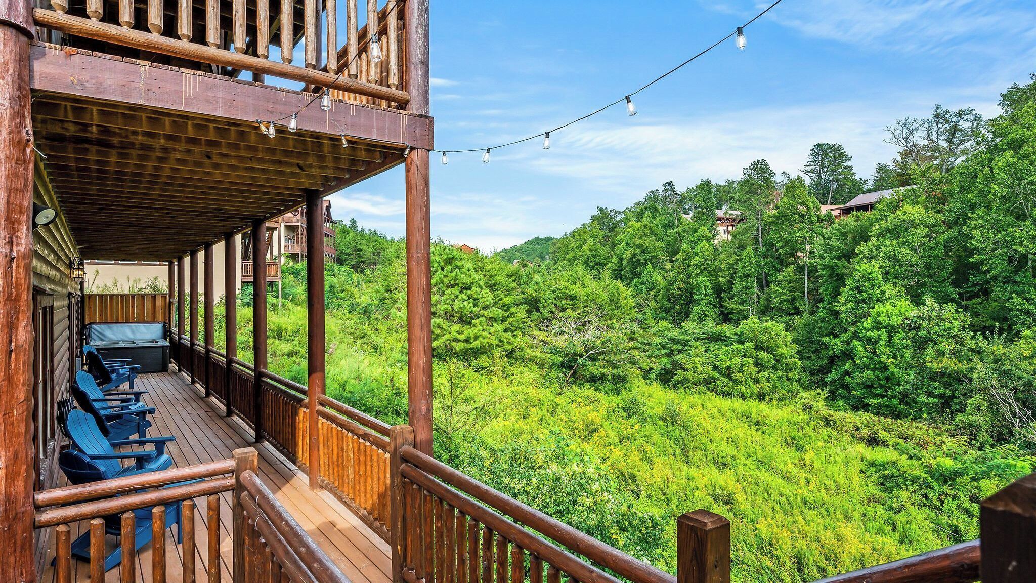 A wooden deck with outdoor seating and a view of a lush green forest.