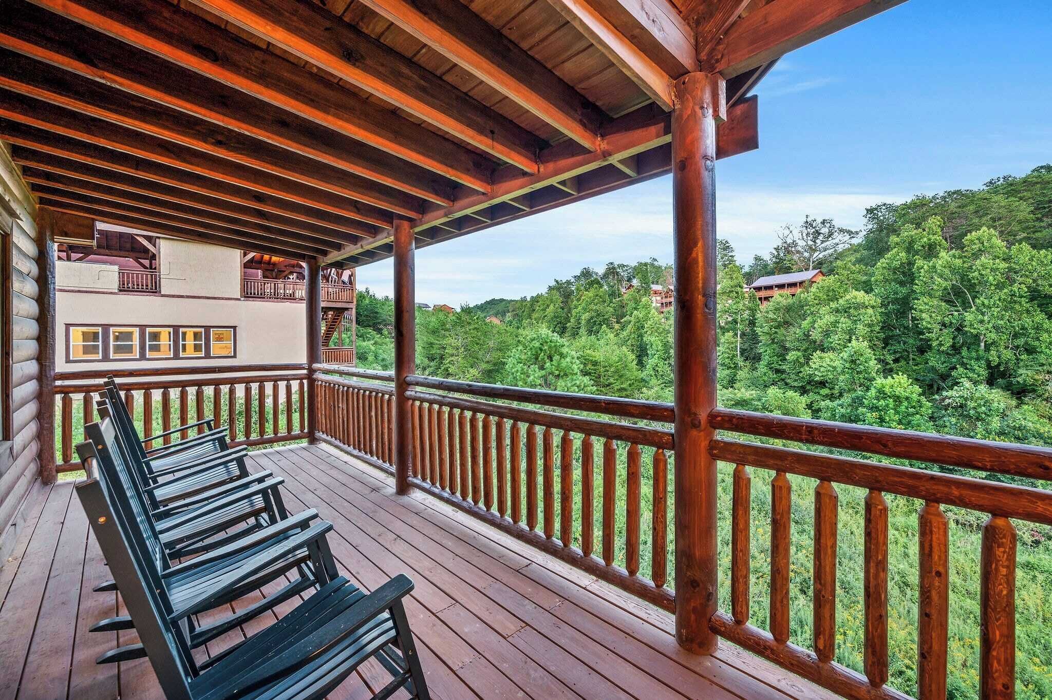 Une terrasse en bois avec des bancs, une rambarde et une vue sur une colline boisée.