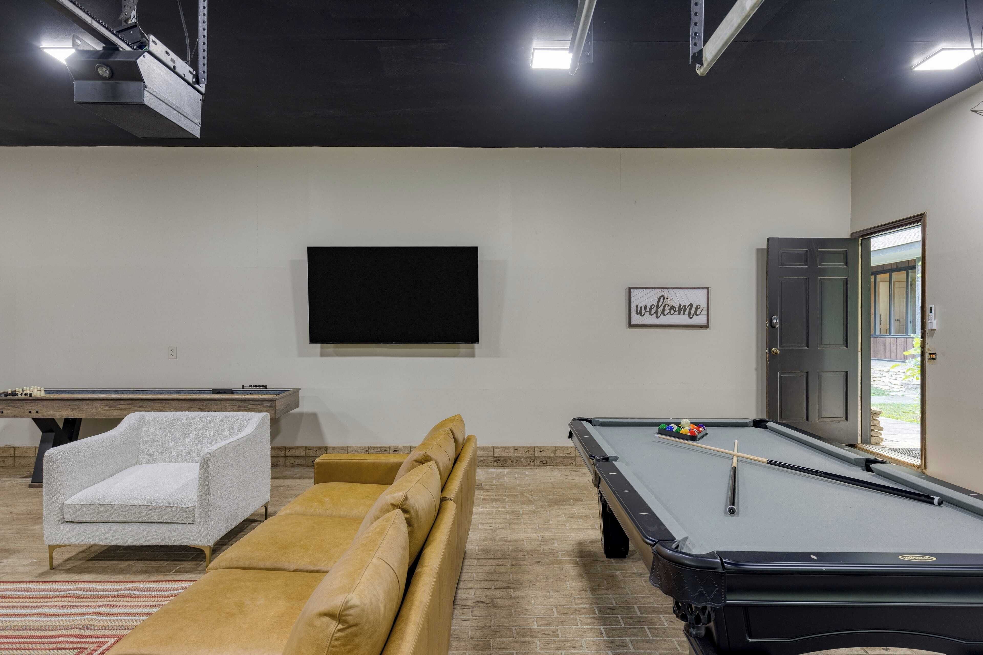 A pool table with a welcome sign, a sofa, and a chair in a room with a brick floor and a door leading outside.