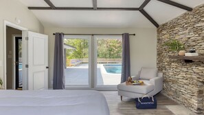 A bedroom with a bed, a sofa, a stone wall, a pool, and a door leading outside. - Amber Refresh by Avantstay Pool and Hot Tub (New Market)