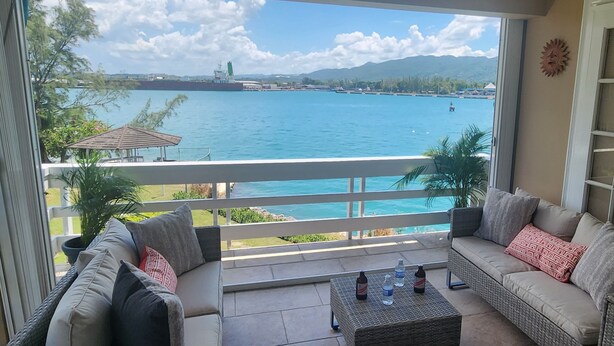 Un balcon donnant sur une vaste étendue d’eau, un coin salon avec un canapé et une table, et une plante en pot.