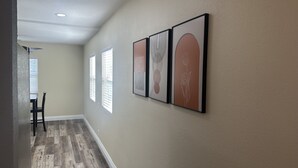 Een gang met houten vloer, een eetgedeelte met tafel en stoelen, en drie kunstwerken in lijsten aan de muur.