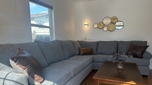 Een moderne woonkamer met een grijze modulaire bank, een houten salontafel en een wandlamp.