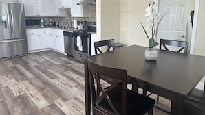 Een moderne keuken met witte kasten, roestvrijstalen apparatuur en een eethoek met een donker houten tafel en stoelen.