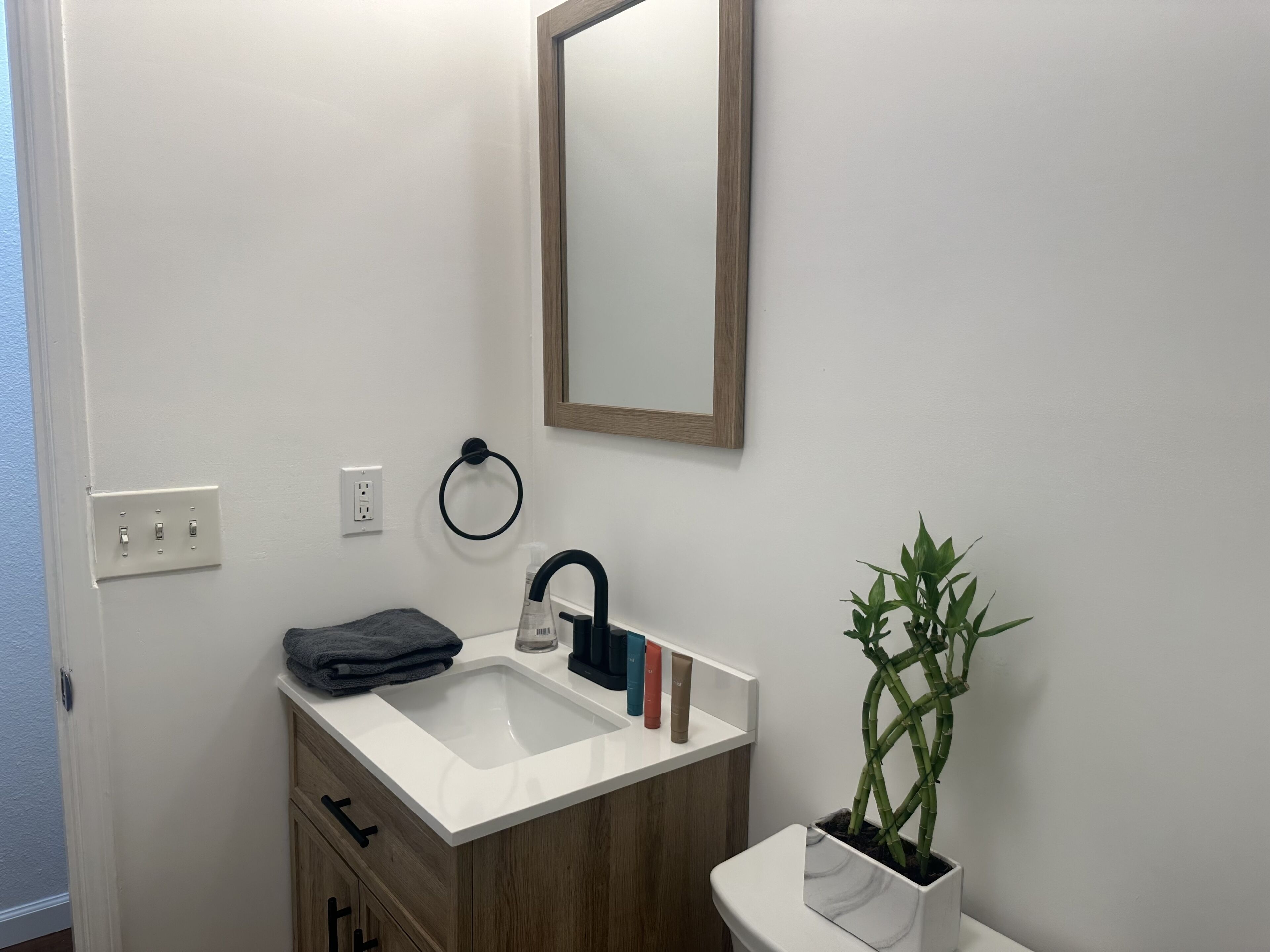 A modern bathroom with a white sink, wooden cabinet, and a mirror.