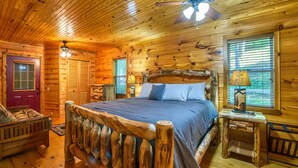 Ein Schlafzimmer in einer Blockhütte mit einem hölzernen Bett, einem Deckenventilator und einem Fenster mit Jalousien.