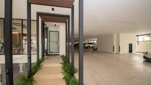 Amplo espaço interno com piso de azulejos, uma galeria coberta com vegetação e área de estacionamento com carros.