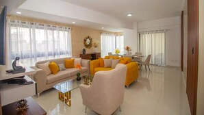 Uma sala de estar moderna com um sofá bege, poltronas amarelas e uma mesa de centro de vidro.