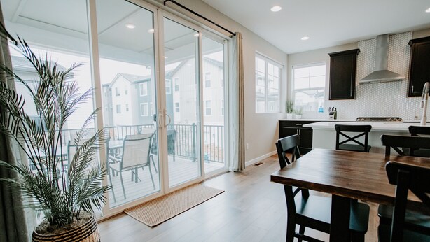 A modern kitchen with a large island, sliding glass doors leading to a balcony, and a potted plant. - New Modern Stylish Oasis, Bright and Comfortable Home (Parker)