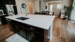A modern kitchen with dark cabinetry, a white countertop, and a stainless steel refrigerator. - New Modern Stylish Oasis, Bright and Comfortable Home (Parker)