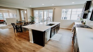 A modern kitchen with a central island, wooden flooring, and large windows. - New Modern Stylish Oasis, Bright and Comfortable Home (Parker)