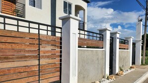 A modern building with a wooden fence, concrete pillars, and a paved pathway with rocks and plants.